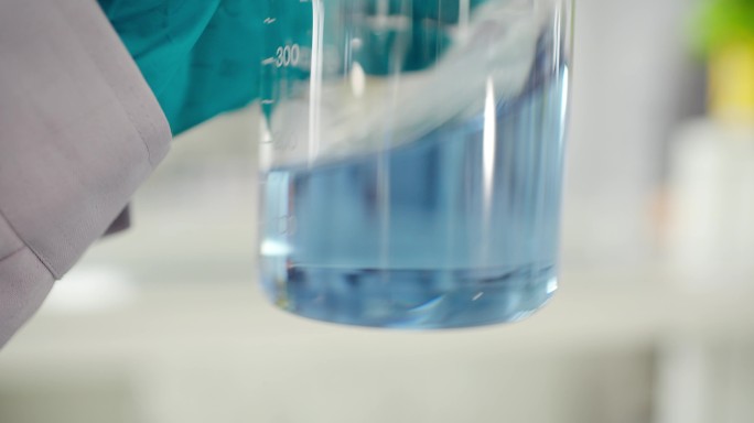 实验人员摇晃观察化学器皿里的蓝色溶液