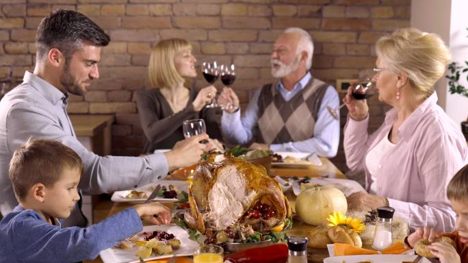 一家人在餐厅举行感恩节晚宴时，用葡萄酒敬酒。
