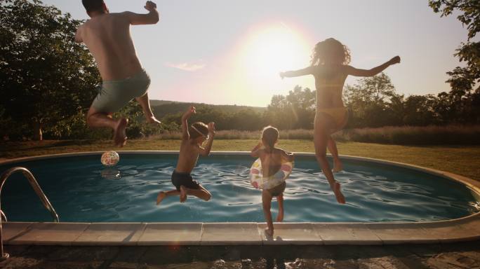 无忧无虑的一家人跳进游泳池的后视图。