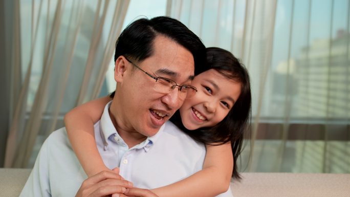 女儿拥抱着父亲，看着摄像机，然后带着愉快的心情对摄像机微笑