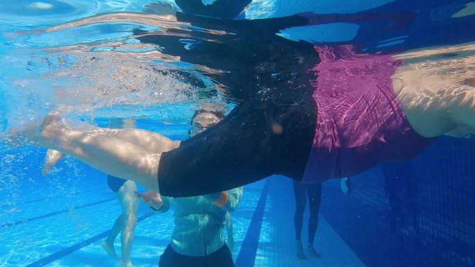 亚裔中国高级女子游泳运动员在游泳教练的指导下在池边练习踢腿