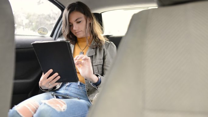 年轻女子在出租车后座使用平板电脑
