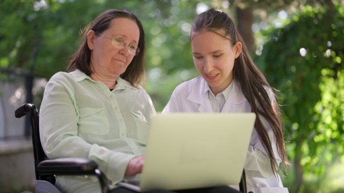 专业女性医护人员教坐轮椅的资深女性如何使用笔记本电脑的特写视频