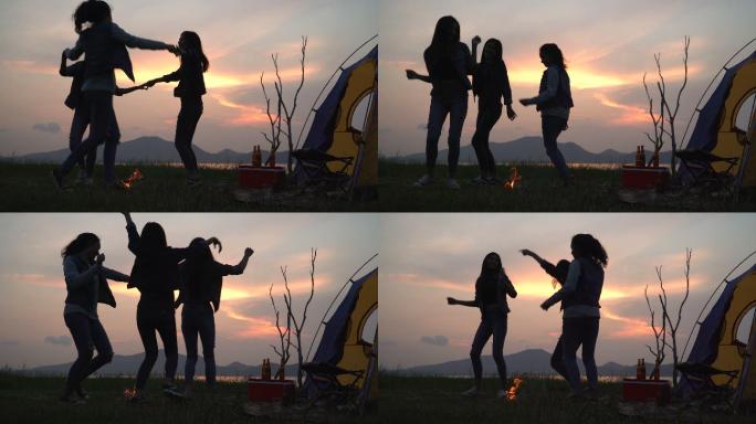 低角度视图：朋友在夏天围着营火跳舞，日落时在湖边露营