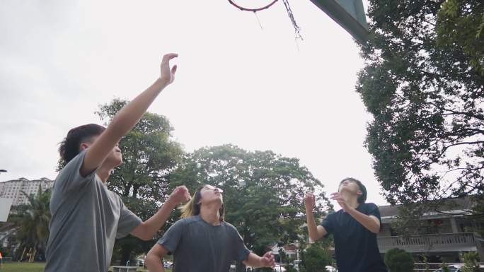 慢动作背光Z代亚裔中国少年在周末早上与朋友练习篮球比赛时挑战球员并投篮