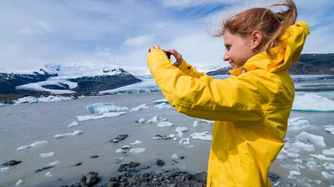 大风天，一名女子在冰河泻湖拍摄浮冰照片