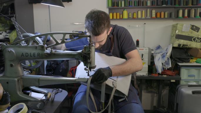 经营小企业的年轻人在缝纫机的皮带扣周围缝制皮革肩带