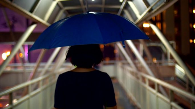 带着雨伞在人行天桥上行走的女性