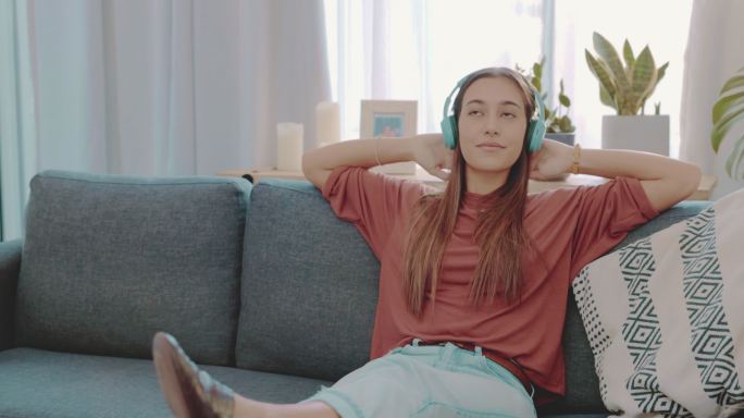 一个迷人的年轻女子独自坐在沙发上，通过耳机听音乐的4k视频片段
