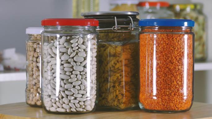 将盛满豆类的玻璃罐从食品储藏室的架子上翻过来