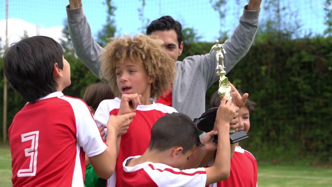 男孩足球队和教练手持奖杯，兴奋地跳起来庆祝他们赢得了锦标赛