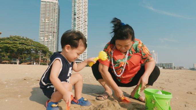 亚洲祖母和孙子在沙滩上玩沙子