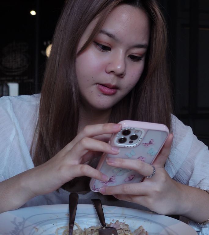 在餐厅吃饭时使用智能手机拍摄照片或视频的亚裔女孩