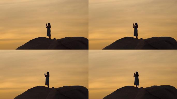 日落时站在岩石上的女孩剪影