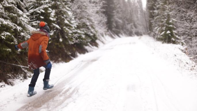 冬日森林里，小男孩在白雪覆盖的道路上滑行