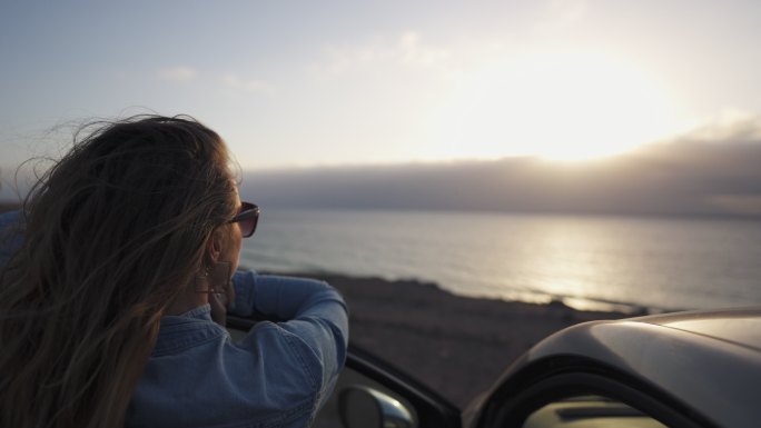 特写镜头中，一名女子在停车时从车上向大海眺望