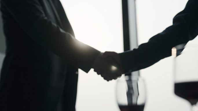两个商人达成协议后握手，旁边放着一个红酒杯