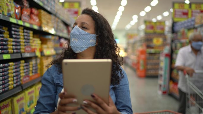 戴口罩的女性使用数码平板电脑控制超市库存