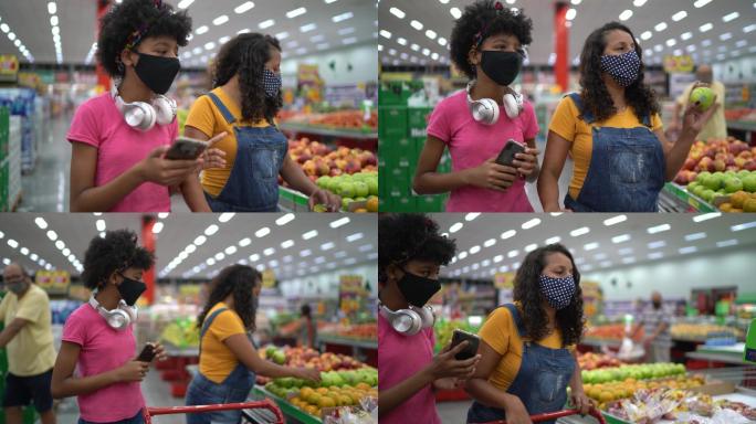 母亲和女儿戴着口罩在超市用智能手机买水果