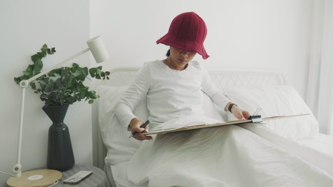 戴红帽的利基女性室内艺术家正在她的白色卧室为她的休闲活动进行绘画和素描