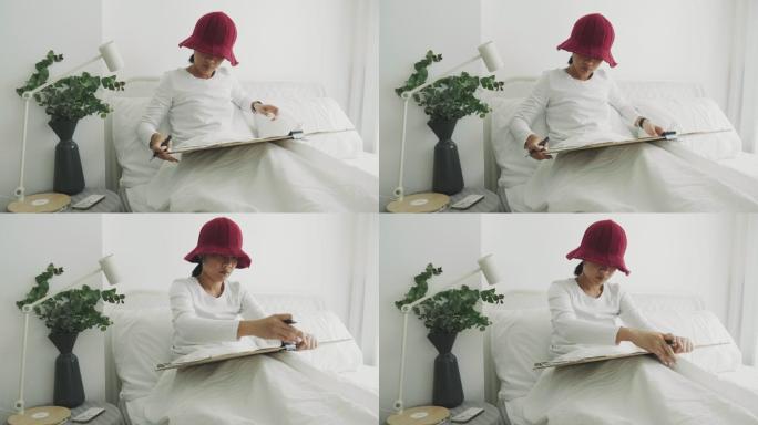 戴红帽的利基女性室内艺术家正在她的白色卧室为她的休闲活动进行绘画和素描