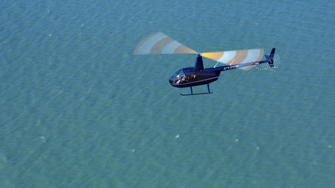 空中直升机在阳光下飞越海面