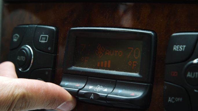 一名白人男子的手指按下汽车仪表板上的温度控制按钮，使驾驶员的体温升高