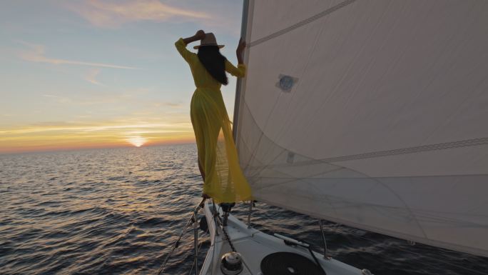 落日时分，斯洛·莫（SLO-MO）女士在享受帆船船头的微风时，把手举在空中