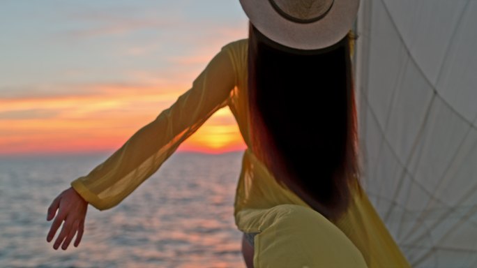 日落时分，身穿黄色长裙的超级懒妇在帆船船头享受微风