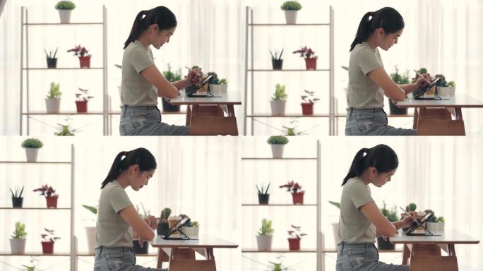 亚洲女性在货架上装饰着植物的客厅里玩平板电脑。