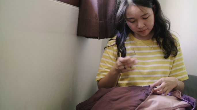一位年轻的亚洲女子用手缝制衣服。