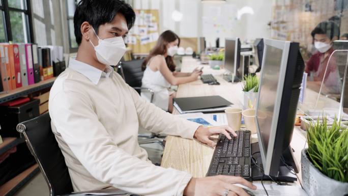 新常态的环境在现代办公室工作2019冠状病毒疾病，亚洲商人通过屏幕分隔与客户和朋友打电话做生意，戴上