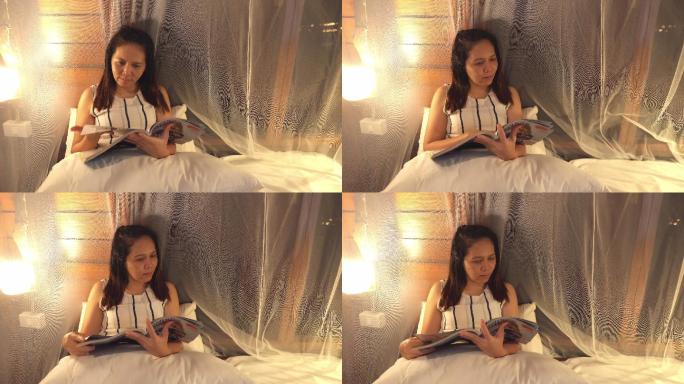 正面图：亚洲女性晚上坐在白色卧室里看杂志，感受积极的情绪，微笑，独处的夜生活理念，放松