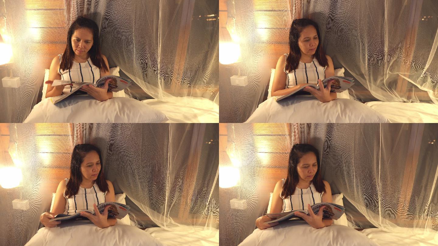 正面图：亚洲女性晚上坐在白色卧室里看杂志，感受积极的情绪，微笑，独处的夜生活理念，放松