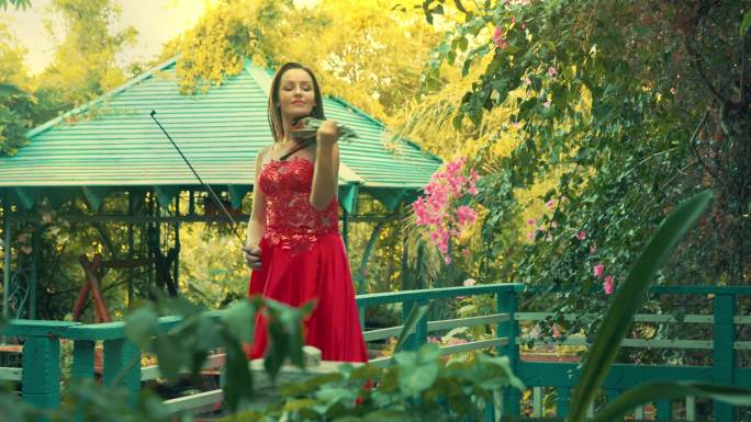 穿着红色衣服的女人在公园的凉亭附近拉小提琴