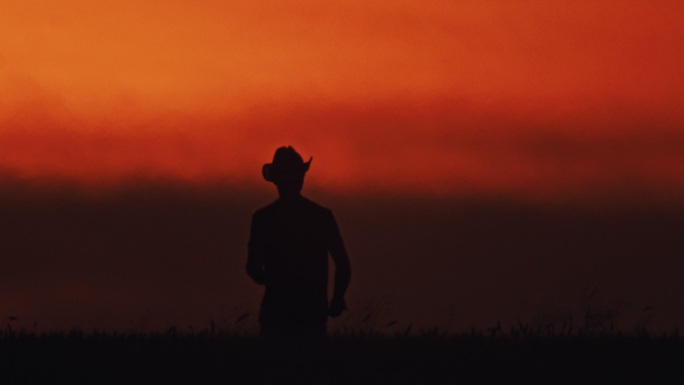 戴着太阳帽的斯洛莫农民站在橙色天空下的麦田里