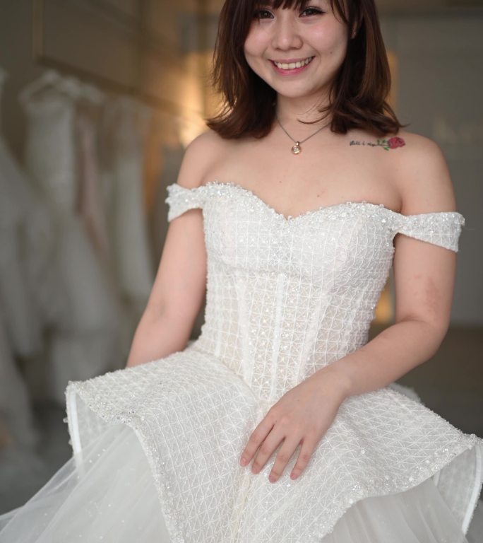 快乐自豪满意的亚洲华人新娘肖像摆姿势看着相机微笑着在婚纱店试穿婚纱