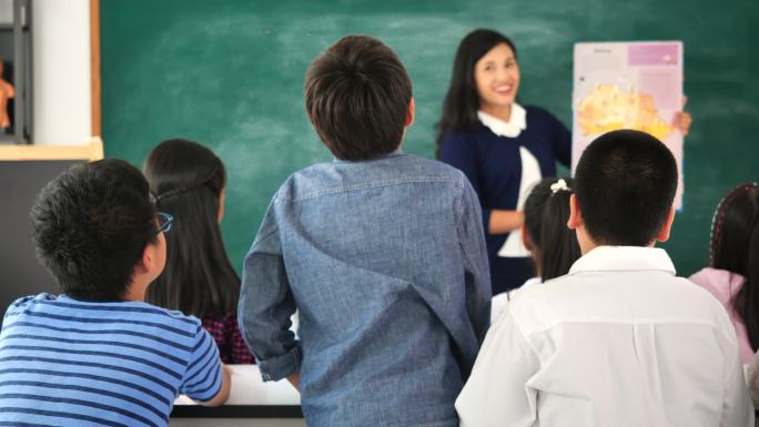 演讲期间，男生站在课堂上举手回答问题的后视图。学生举手向讲师提问。