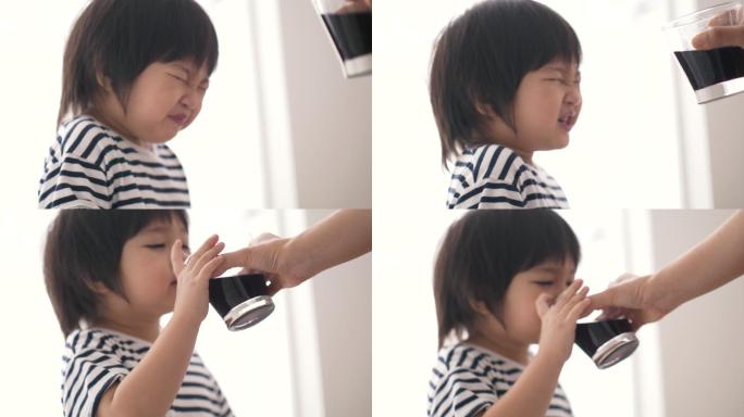 一个小男孩一边喝葡萄汁一边表情滑稽不好吃