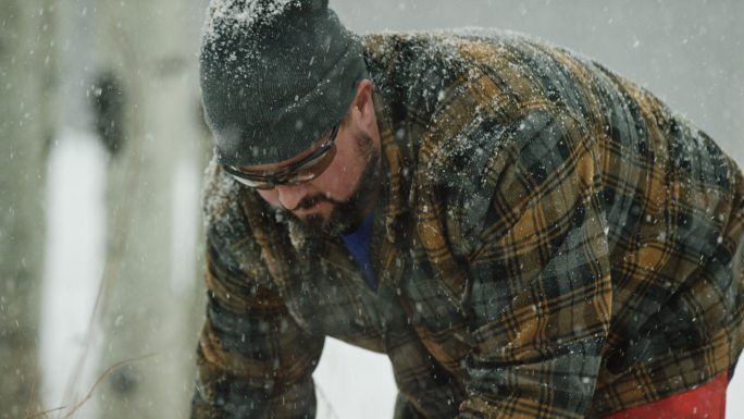 在一个下雪的冬日，一名30多岁留着胡子的白种人用电锯砍断了一根白杨木