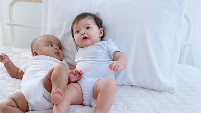 两个可爱的黑白相间的新生男孩躺在白色的卧室里，快乐地玩耍、交谈、交叉着双腿。