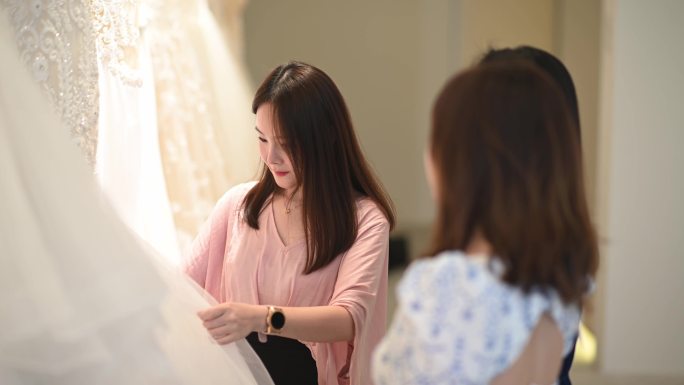 中国亚裔女性婚纱店老板向顾客解释新娘婚纱系列