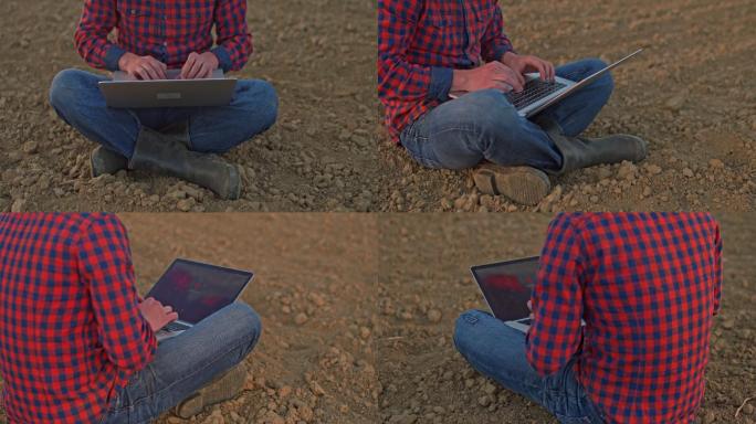 中景：Farmer坐在田园诗般的农村耕地上，使用笔记本电脑