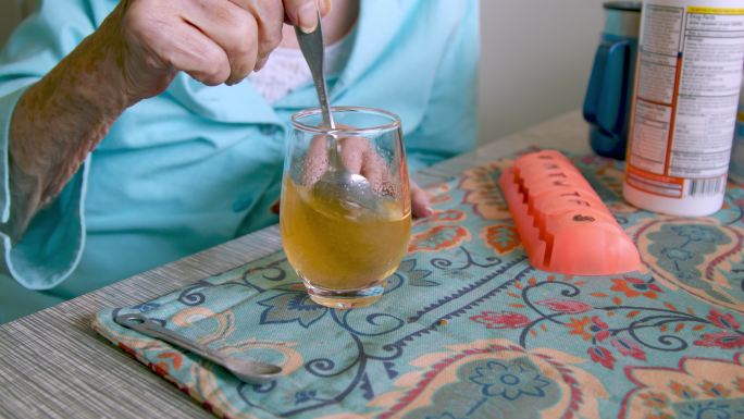 老年妇女搅拌溶解橙色粉末饮料混合物，用于日常维生素补充剂或药物治疗