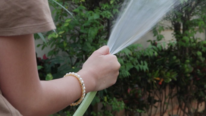 4K，女孩手持式浇水软管和花园浇水树
