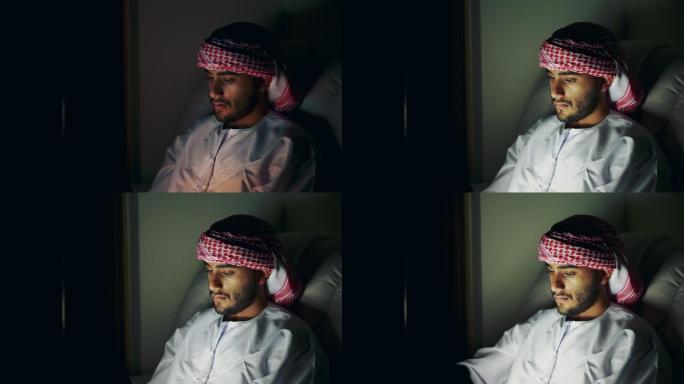 阿拉伯年轻人坐在黑暗的房间里使用数字平板电脑上网