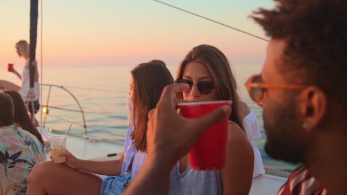 日落时分，斯洛·莫（SLO MO）男男女女在游艇上的派对上碰杯
