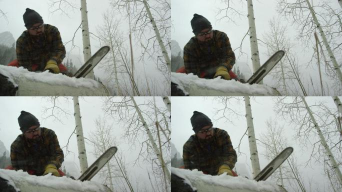 一位30多岁留着胡子的高加索人在大雪纷飞的冬日里，用电锯在山上锯一根白杨木原木