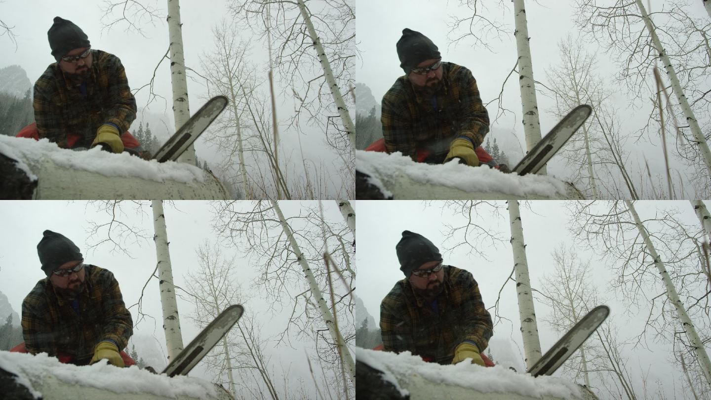 一位30多岁留着胡子的高加索人在大雪纷飞的冬日里，用电锯在山上锯一根白杨木原木