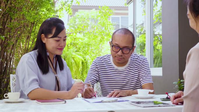 幸福的亚洲成年夫妇坐在家里的前院或后院与保险代理人谈判签订合同